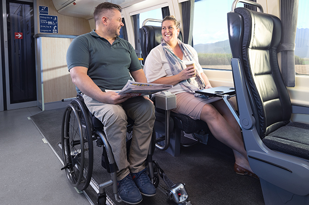 A customer sits in their wheelchair in the Carriage E Accessible Wheelchair Space. with a companion sitting beside in a seat.