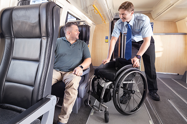 A team member assists a seated customer with their wheelchair to be stored.