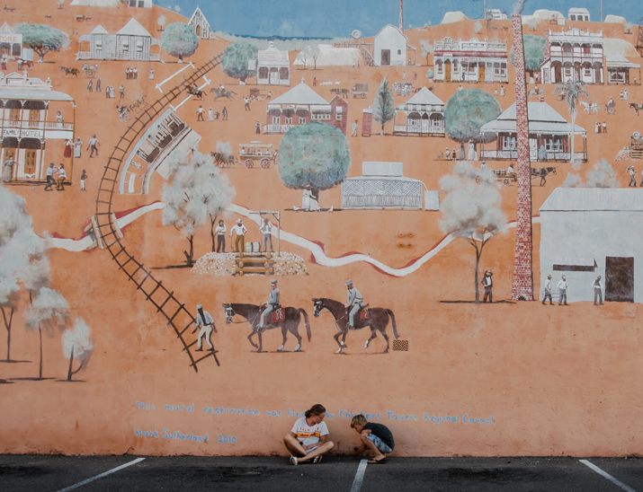 Two people sitting on the ground in front of a mural