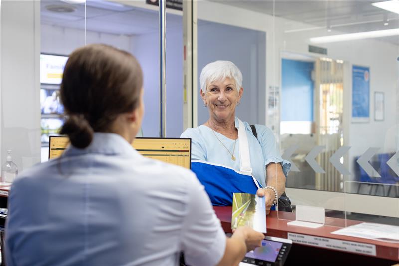 A customer with an arm in a sling being served by a Queensland Rail Travel team member at a ticket office.