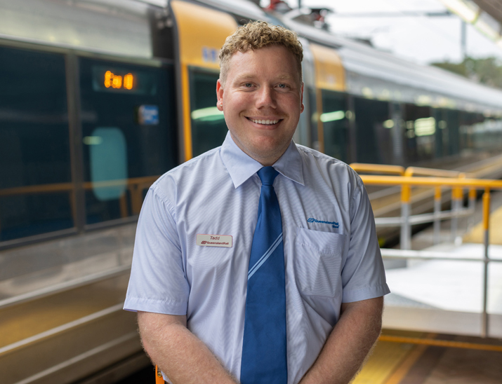 A Queensland Rail Travel team member  standing on the train platform smiling and ready to offer assistance